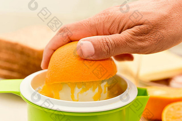特写镜头：一名白人年轻男子用塑料挤压器挤压橙子，为早餐准备新鲜橙汁