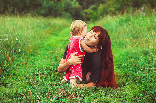 美丽的年轻的妈妈。女儿放松坐着草<strong>背景</strong>夏天草地绿色草树