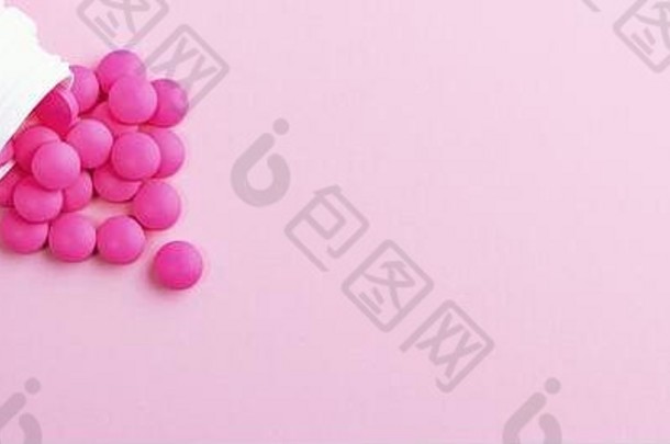 白色药瓶里散落着亮粉色的药丸。在粉红色背景上隔离
