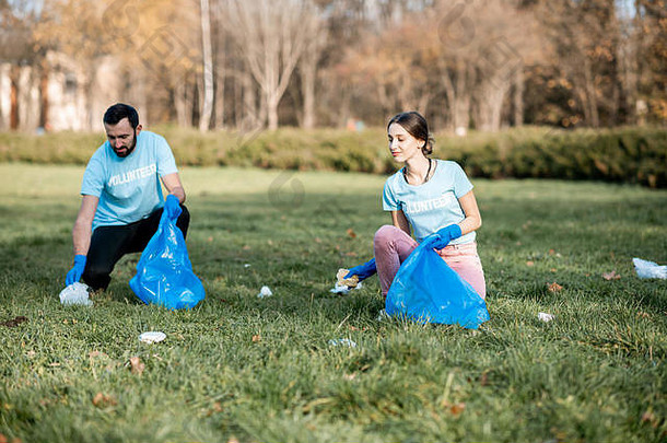 穿着蓝色t恤衫的快乐男女志愿者正在清洁公共花园，将塑料垃圾放入袋子中