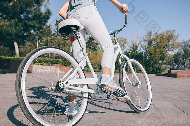 体育女孩牛仔裤运动鞋坐在自行车城市