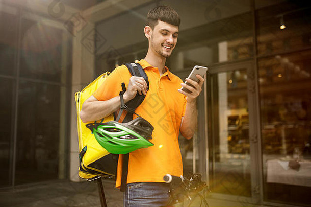 一名身穿黄衬衫的年轻人正在运送包裹，他使用小工具跟踪城市街道上的秩序。使用在线应用程序接收和跟踪发货地址的快递员。现代技术。