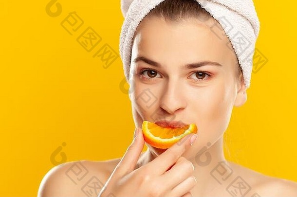 在黄色背景上吃橘子的年轻漂亮女人的肖像