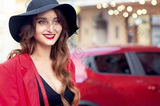 在红色汽车的背景上，一位戴着黑帽子、面带微笑的年轻女子。