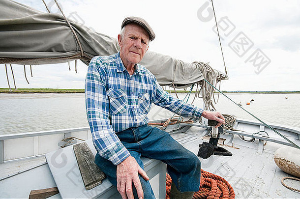 渔夫坐在有桅杆和帆的船甲板上