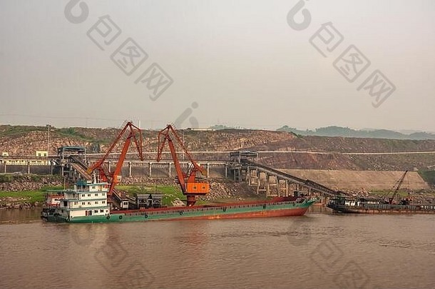 中国重庆——2010年5月8日：长江。红色起重机将煤炭从船上卸到发电厂的运输带上，在李河下宽阔的棕色水域后面