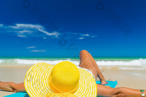 穿着比基尼的女人戴着黄色帽子在热带海滩晒太阳