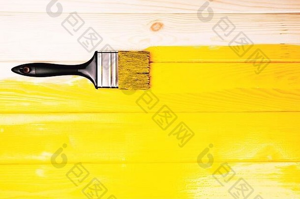 带有黑色手柄的画笔，位于黄色半新涂漆的木质背景上。修复概念。