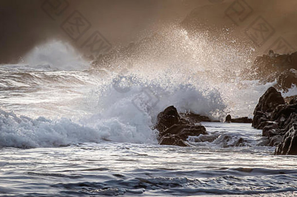 英国南威尔士彭布罗克郡海岸的金色日落。飞溅的波浪和晚风，悬崖和薄雾的背景。<strong>英国风景</strong>名胜区。泼洒