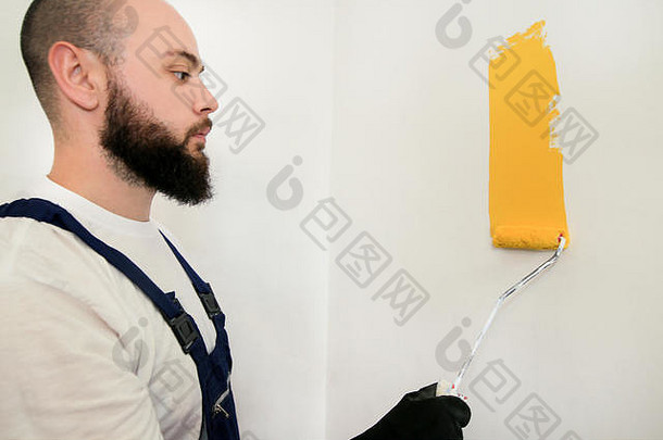 建筑工人和杂工正在完成公寓的装修。油漆工用油漆滚筒刷涂黄色墙面。