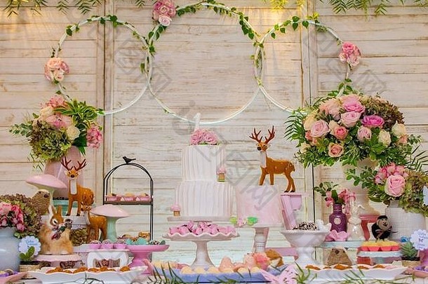 豪华的糖果和生日蛋糕桌上装饰着插花和精致的野生动物，背景是轻质木板。博