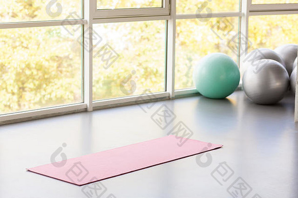 瑜伽垫躺在靠近窗户和健身球的灰色地板上。摄影棚拍摄