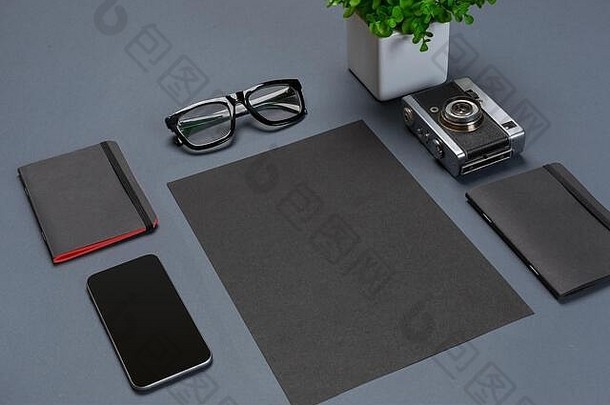 一套黑色办公配件、眼镜、绿色花朵和灰色背景上的智能手机