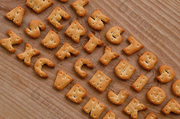 咸饼干的字母排列在木制的棕色表面上，排列顺序与电脑键盘上的按钮布局相似。滑稽模仿