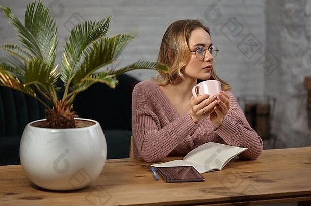 女人眼镜粉红色的开襟羊毛衫持有杯坐着木表格平板电脑笔记本花能学生博主特写镜头