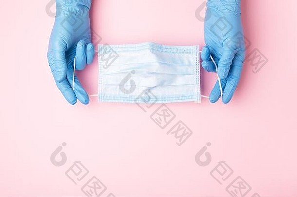 手戴蓝色手套，粉红色背景上显示医用面罩。防止病毒感染的预防措施。