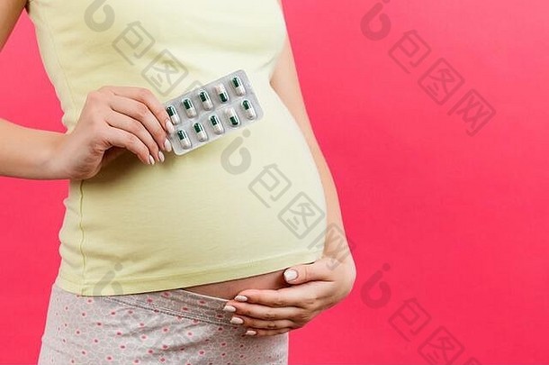 孕妇手上的药丸水泡贴在腹部的特写镜头，背景色彩丰富，有复印空间。怀孕期间的维生素概念。
