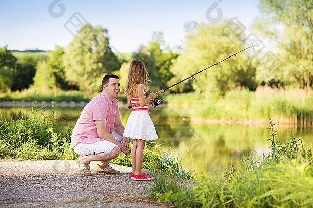 快乐的年轻父亲和他的小女儿在湖边钓鱼