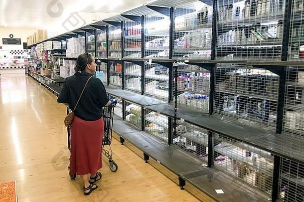 2019冠状病毒疾病爆发。一名妇女站在超市的空货架上，担心冠状病毒大流行。<strong>抢购</strong>使得杂货店空无一人