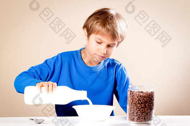 孩子在吃早餐。男孩把牛奶倒进一<strong>碗</strong>麦片粥里