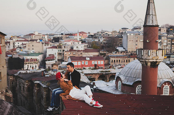 相爱的情侣坐在屋顶上欣赏伊斯坦布尔的夜景。休闲风格，秋季造型，红色贝雷帽和米色外套