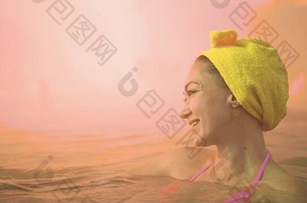 特写镜头：一名白人妇女在传统的户外温泉浴场游泳，沐浴在温暖的盐水中，沐浴着柔和的神奇粉色灯光蒸汽。地热温泉。