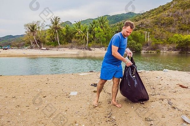 戴手套的人捡起污染海洋的塑料袋。人为污染造成的海滩沙上垃圾溢出问题及对策