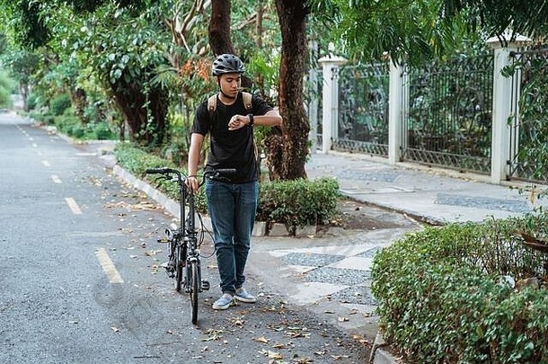 亚洲年轻人一边在街上看手表，一边骑着<strong>折叠自行车</strong>走路