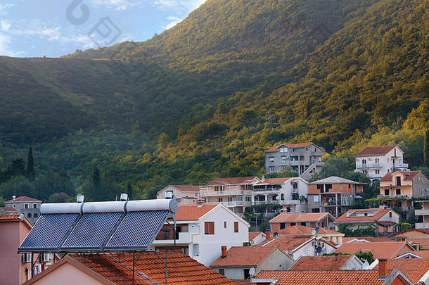 现代可再生太阳能<strong>热水器</strong>在房子的橙色瓦片屋顶上，背景是黑山的山区景观
