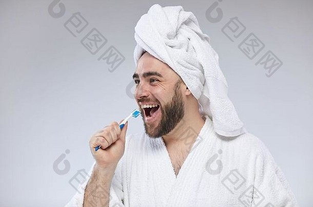 水平摄影棚的肖像画，滑稽的胡子男人穿着白色<strong>浴</strong>衣和毛巾头巾，用牙刷代替麦克风唱歌