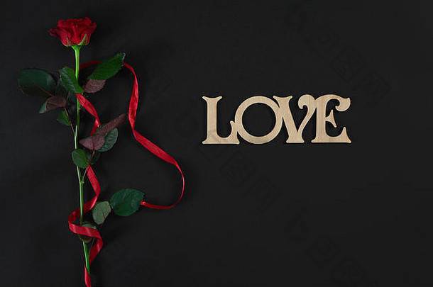 一朵深红色的玫瑰，黑色背景上有红丝带。浪漫的情人节假期概念。情人节贺卡。
