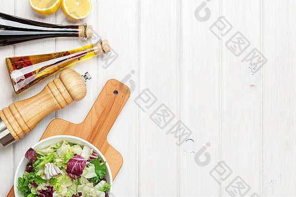 白色木桌上放着新鲜健康的沙拉和调味品。使用空间从上方查看