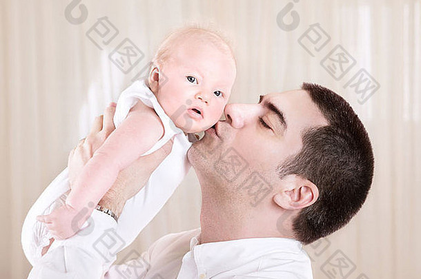 英俊的爸爸接吻可爱的蹒跚学步的男人。享受时间花新生儿女儿首页爱概念