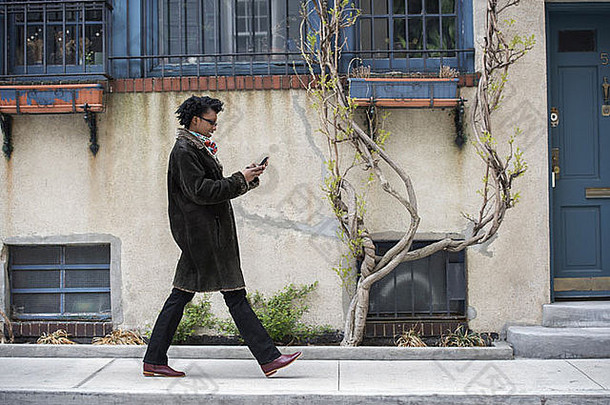 一个穿着暖和外套的女人在街上走着检查她的手机