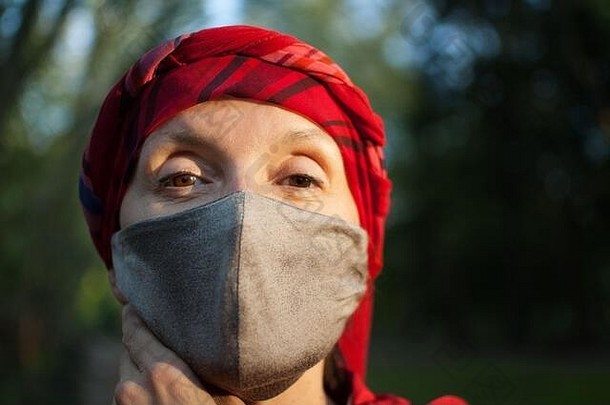 由于冠状病毒的影响，在阳光明媚的春天，公园里的成年妇女戴着手工织物面罩作为配饰和保护元素