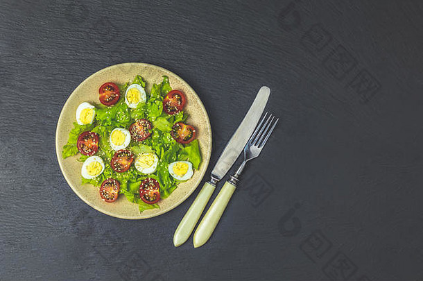 新鲜健康沙拉，生菜，鹌鹑蛋，樱桃番茄和芝麻放在盘子里。俯视图，空间。