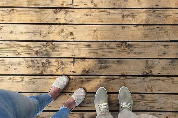 两个人站在一个木头表面上。穿着浅色夏装鞋的脚的俯视图