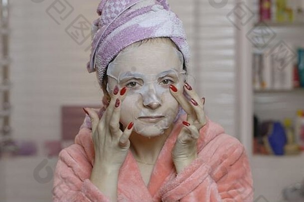 一名妇女在浴室里戴着化妆面罩，看着摄像机。照顾脸部皮肤的女孩。<strong>护肤</strong>水疗。<strong>面膜</strong>