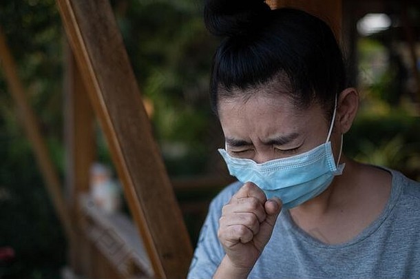 一位站在公园里准备戴上医用口罩的亚洲年轻女子在模糊的背景下咳嗽