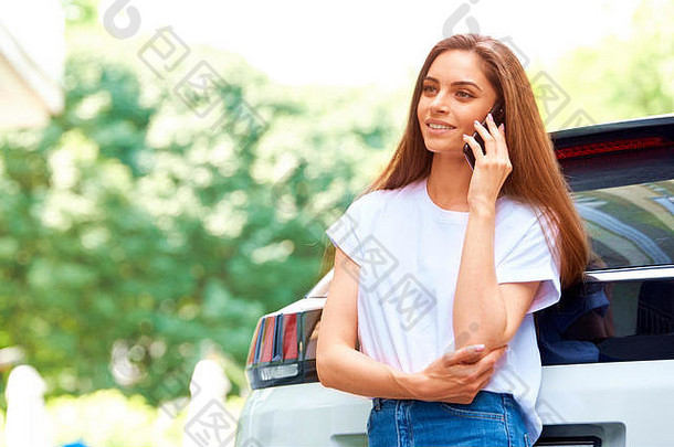 这张照片拍摄的是一位休闲的年轻女子站在车旁的街道上用手机与人交谈。