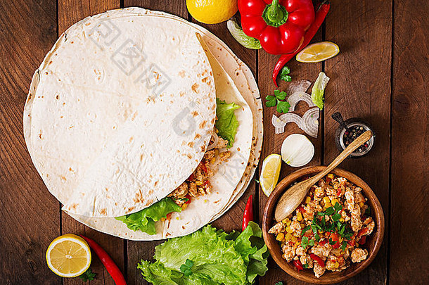 墨西哥煎饼的配料是在木质背景上包裹鸡肉、玉米、西红柿和辣椒。俯视图