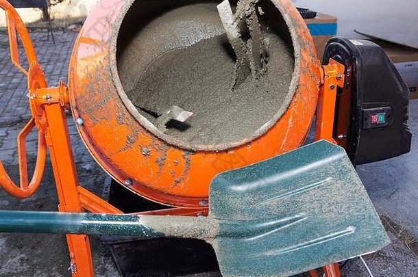 建筑工人把沙子铲进混凝土搅拌机。在施工现场水泥的过程