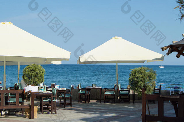 在一个阳光明媚的夏日，海边餐厅的桌子和雨伞