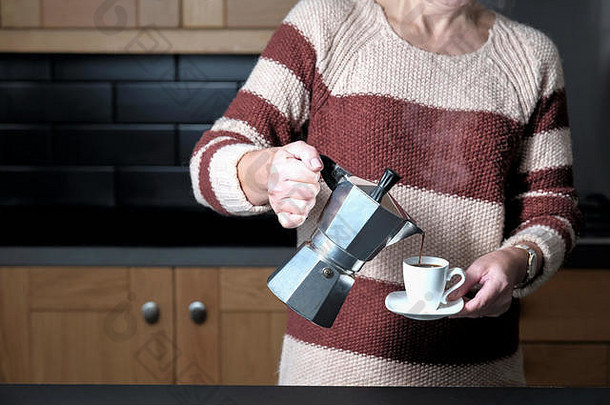 一个聪明但穿着随意的女人站在家里的厨房里，从摩尔霍布咖啡壶里倒咖啡