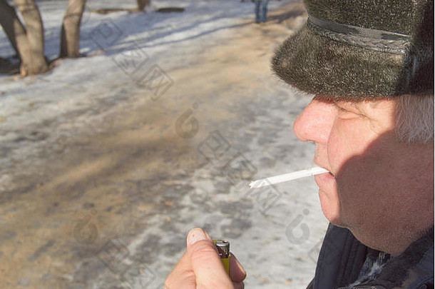 特写镜头：一位头发灰白的老人，手拿香烟和打火机，背景是冬天。