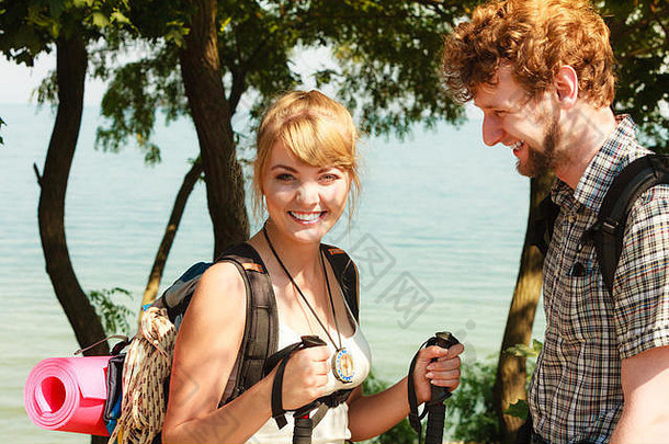 两个年轻人在海边徒步旅行。背包客夫妇在暑假旅行。拿着登山杖的女人。