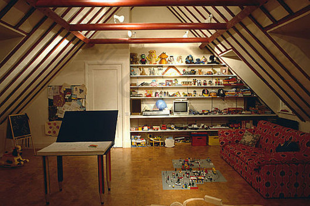 阁楼转换游戏室中的红色沙发和软木地板，带有梁顶天花板和木制火车套件