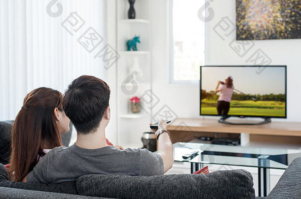 亚洲年轻夫妇在家里电视上观看高尔夫运动