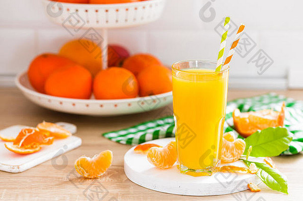 在白色木制厨房背景特写镜头上，有装在玻璃杯中的橘子汁和带叶子的新鲜水果。健康可口的夏日清爽饮料