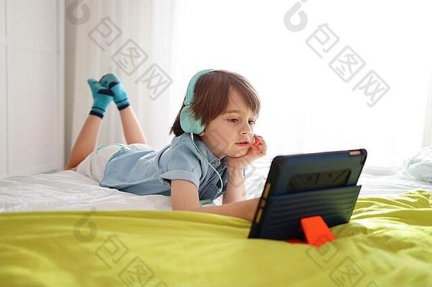 放松的小男孩在家里用耳机和平板电脑在线上<strong>课</strong>。隔离<strong>期间</strong>的社会距离与<strong>网</strong>络教育理念